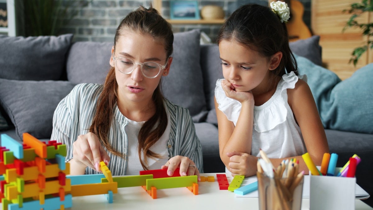 Cute little girl playing at home with caring mother having fun with wooden toys enjoying family activity. Childhood, motherhood and apartment concept.